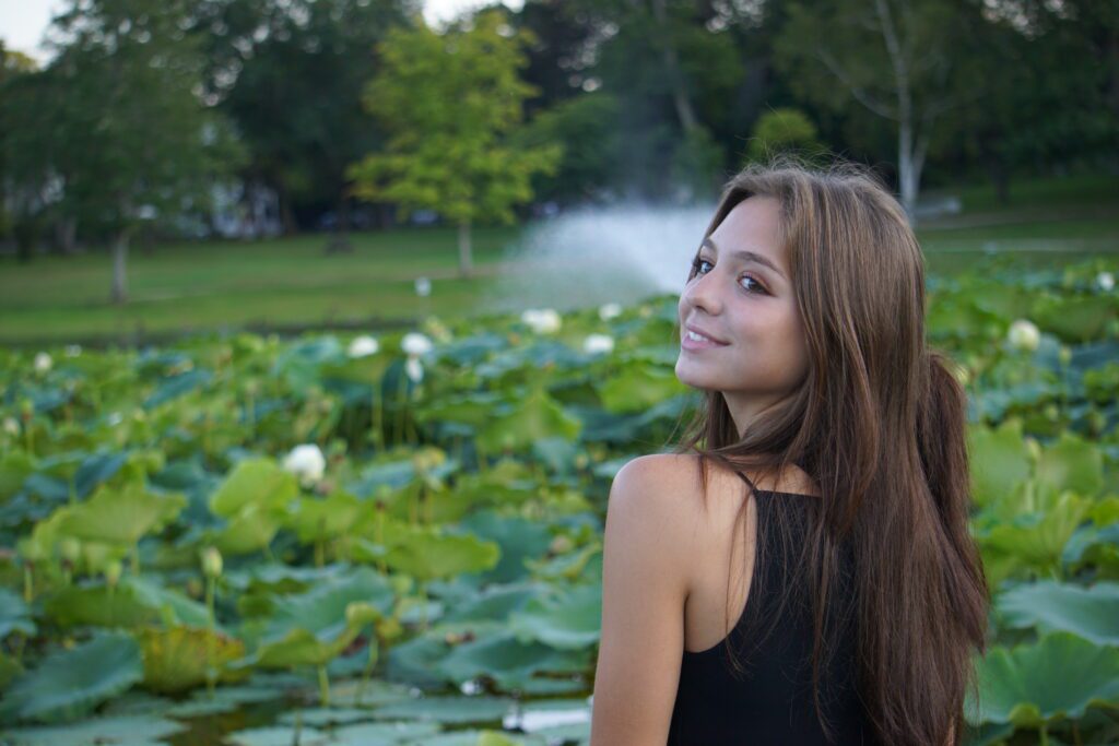 Brunette smiling with a pond and fountain in background.